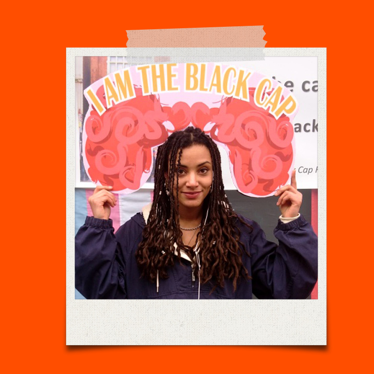 A young woman holding a I am The Black Cap banner